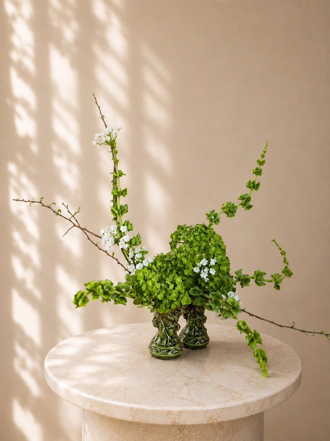 Green and white sculptural floral vessel arrangement on a marble plinth